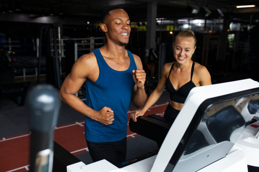 Homme et femme courant sur tapis de course en salle, encadrés par un coach sportif à Yvetot