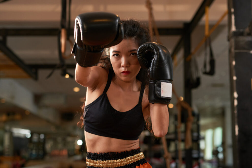 Femme en position de garde avec gants de boxe noirs dans une salle de sport, pratiquant la boxe fitness à Yvetot